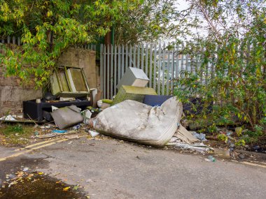 Terk edilmiş çöp ve mobilyalar, yatak ve televizyon da dahil, çitin yanındaki zemini kirletiyor..