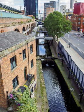 Manchester, İngiltere. 28 Eylül 2024: Tuğla binalar ve yeşilliklerle kaplı pitoresk şehir kanalı.