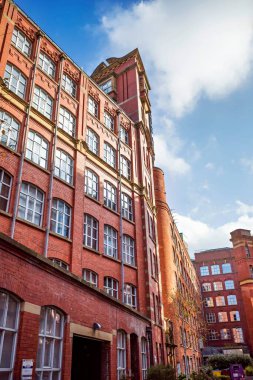 Historic red brick mill building with tall windows under a clear blue sky. Manchester city center. clipart