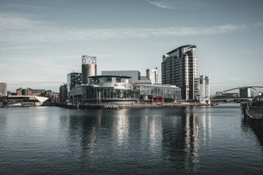 Modern mimari berrak bir gökyüzünün altındaki sakin sulara yansıdı. Salford Manchester Quays.