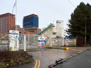 Salford, Manchester, UK. January 04, 2025: A Cemex industrial site featuring construction equipment, including cement silos, with urban buildings visible in the background. clipart