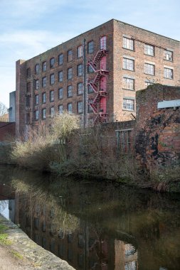 Sakin bir kanalın yanındaki kırmızı yangın çıkışlı tarihi tuğla bina..