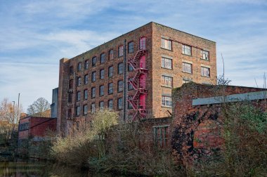 Açık bir günde suyun yakınında kırmızı yangın merdiveni olan tarihi tuğla fabrikası..