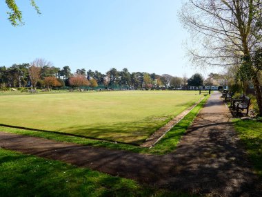 Güneşli bir günde yemyeşil bovling sahası ve banklarla huzurlu park manzarası.