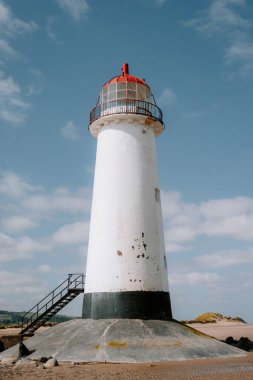 Güneşli bir günde açık mavi gökyüzünün altında, dağınık beyaz bulutlu, uzun beyaz bir deniz feneri..