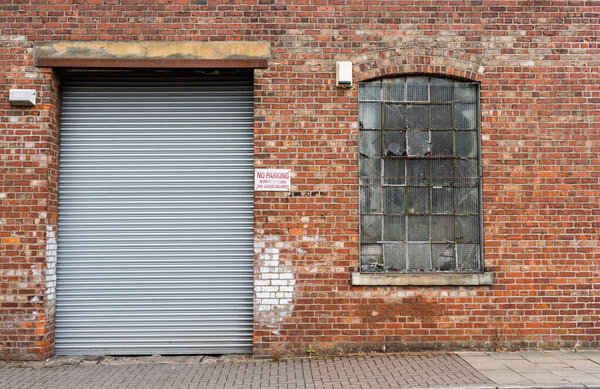 Industrial building with a brick facade with large metal security door and worn wire mess covered window