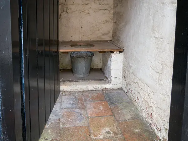 Ahşap bankı ve metal kovası olan taşralı açık tuvalet..