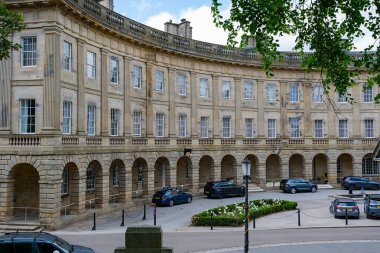 Buxton, Derbyshire, İngiltere, 28 Haziran 2025: Park etmiş arabaları ve yemyeşil yeşillikleri olan tarihi hilal binası Buxton.