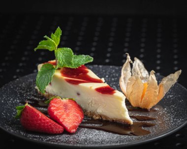 Siyah tabakta taze çilekle süslenmiş cheesecake.