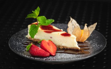 Siyah tabakta taze çilekle süslenmiş cheesecake.