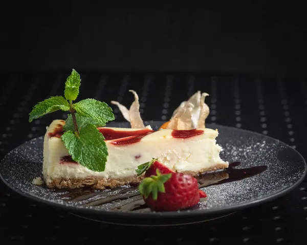 cheesecake decorated with fresh strawberry on a black plate