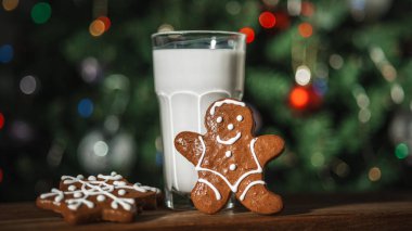 Bir bardak sütle zencefilli çörek ve arka planda ışıklarla süslenmiş bir Noel ağacı.