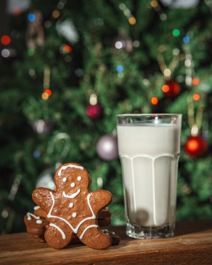 Bir bardak sütle zencefilli çörek ve arka planda ışıklarla süslenmiş bir Noel ağacı.
