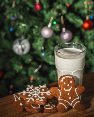 Bir bardak sütle zencefilli çörek ve arka planda ışıklarla süslenmiş bir Noel ağacı.
