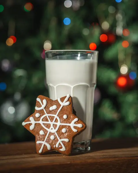 Bir bardak sütle zencefilli çörek ve arka planda ışıklarla süslenmiş bir Noel ağacı.