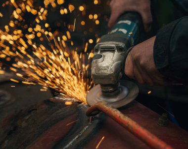 İşçi atölyede kıvılcımlar saçan metal bir yapı öğütüyor.