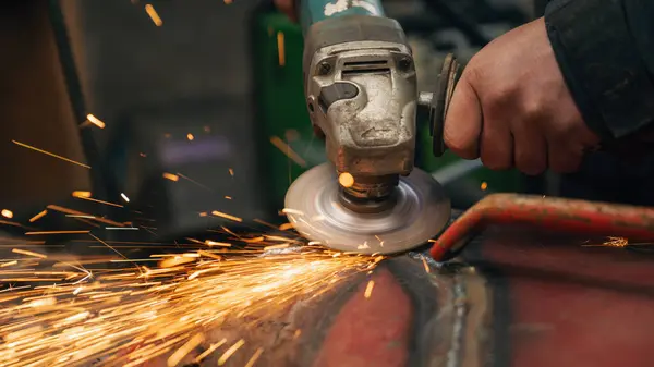 İşçi atölyede kıvılcımlar saçan metal bir yapı öğütüyor.