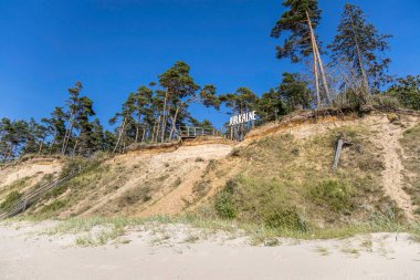 Jurkalne tabelası. Baltık kıyılarındaki dik yamaç ve çam ormanı manzaralı..