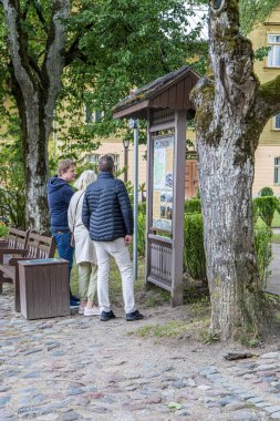 Kuldiga, Letonya - 3 Temmuz 2023: Uyarı panosuna bakan turistler.