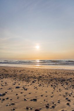 Gün batımında kum ve çakıl taşlarıyla aydınlık deniz..