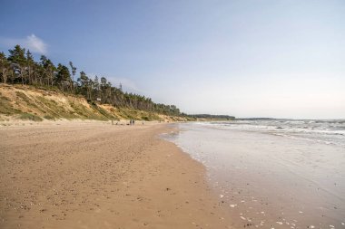 Dik kayalıkları ve uzak mesafedeki insanlarla dolu Jurkalne plajı..