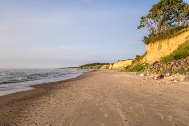 Dik kayalıkları ve uzak mesafedeki insanlarla dolu Jurkalne plajı..