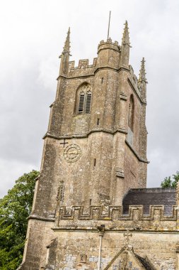 Avebury, UK- 25 Ağustos 2024: Avebury Kilisesi M.S 1000 yılından kalma ve Wiltshire 'daki Avebury Malikanesi yakınlarında yer almaktadır. Bir kadın kilisenin yanındaki bankta oturuyor..