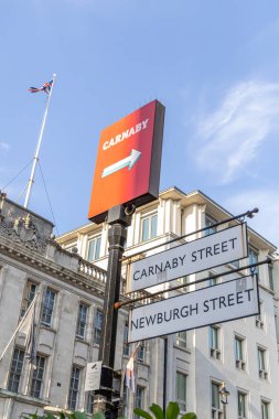 London, UK- September 19, 2024: Red Carnaby Arrow Sign and Union Jack Flag - London s Shopping Landmark. clipart