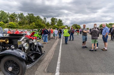 Llandow, Wales - June 30, 2024: A vibrant classic car show with vintage vehicles and enthusiasts socializing at Llandow Circuit. clipart