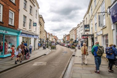 Wells, UK- August 4, 2023: Busy main street with people, coffee shops and other businesses and entrance to the Bishops Palace. clipart