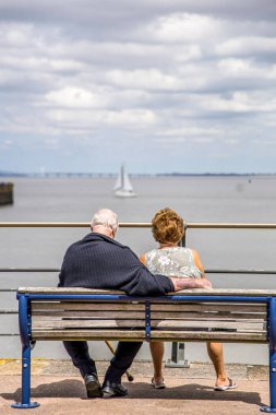 Portishead, UK- 10 Ağustos 2023: yaşlı bir çift bankta oturuyor ve yatların açılmasını izliyor. Galler Köprüsü ve Galler Prensi kadar uzakta..