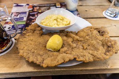 Hamburg, Almanya - 17 Haziran 2024: Patates kızartmalı ve ahşap masadaki soslu sosis şnitzel.