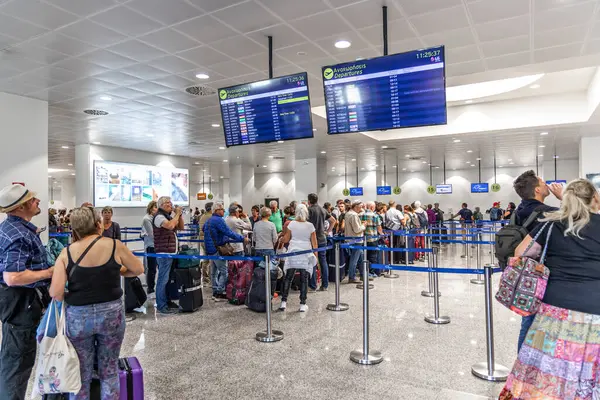 Santorini, Yunanistan - 21 Ekim 2024: yolcu ve bavullarla dolu Santorini Havaalanı kalkış salonu. Kontrol gişelerinin üzerindeki geniş uçuş bilgileri ekranları