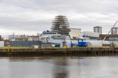 Glasgow, UK- 30 Mart 2024: Glasgow tersanesinde inşaat halindeki donanma gemisi nehir kıyısındaki iskeleleri ve vinçleri ile