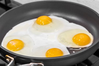 Dört yumurta, siyah tavada kızartılıyor. Yumurta sarısı canlı sarıdır, pişmiş yumurta beyazlarıyla çevrilidir. Tavadan buhar yükselir ve ağız sulandırıcı bir koku yaratır..