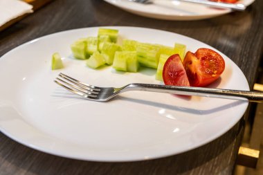 Üzerinde çatal olan temiz beyaz bir tabak. Birkaç dilim domates ve salatalık tabağa saçılmış..