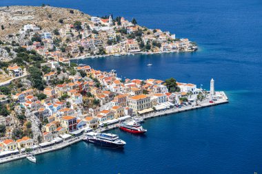 Symi, Yunanistan - 10 Mayıs 2024: Suriye Adası 'ndaki renkli evler köyü ve gemileriyle park halindeki Symi Marina Körfezi' nin bir tepesinden manzara.