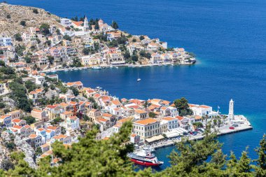 Symi, Yunanistan - 10 Mayıs 2024: Suriye Adası 'ndaki renkli evler köyü ve gemileriyle park halindeki Symi Marina Körfezi' nin bir tepesinden manzara.