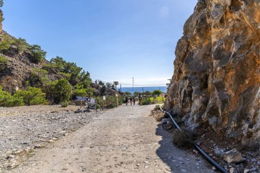 Girit, Yunanistan - 18 Ekim 2024: Samiriye Vadisi 'nin sonu Agia Roumeli kıyı köyüne giden yol, kayalık uçurumların ötesindeki deniz manzarasını ve yolu gösteren işaretler..