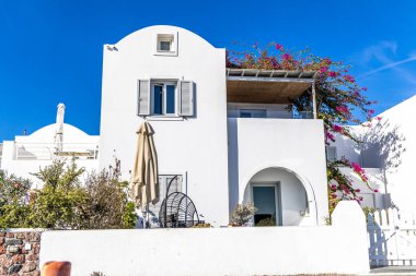 Santorini, Yunanistan - 15 Ekim 2024: Bougainvillea çiçekleri ve büyüleyici ayrıntılarla Santorini 'de beyazlatılmış ev, tipik Yunan mimarisini gözler önüne seriyor.