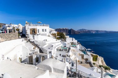 Santorini, Yunanistan - 15 Ekim 2024: Geleneksel beyaz evler ve teraslarla Oia 'dan Santorini' nin büyüleyici manzarası, Ege Denizi ve kaldera manzarası.