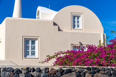 Bir Santorini villasının zarif mimarisi kıvrımlı bir çatısı var ve etrafı çiçek açan begonvillerle çevrili, adanın imzalı bir tasarımı.