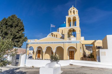 Oia 'daki güzel Agios Georgios Kilisesi. Parlak sarı bir cephesi ve Ege Denizi manzaralı mavi kubbeleri var.