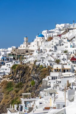 Santorini, Yunanistan - 15 Ekim 2024: Beyaz boyalı evleri ve kayalık bir uçurumda mavi kubbeli bir kilisesi olan Santorini köyü. Geleneksel Yunan adası cazibesi