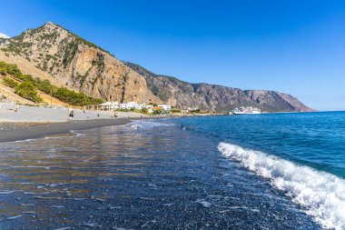 Girit, Yunanistan - 18 Ekim 2024: Girit 'teki Agia Roumeli kıyı manzarası sahilin üzerinde yükselen Samaria Gorge uçurumları ve uzak güney köyü yakınlarındaki feribotlarla