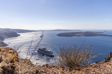 Santorini, Yunanistan - 15 Ekim 2024: Santorini Kalderası 'ndaki Norveç Viva yolcu gemisinin Yunanistan' daki açık yaz gökyüzü altında Nea Kameni volkanı adası ve uçurum kenarındaki kıyı şeridi manzarası.