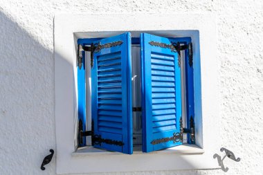 Geleneksel mavi ahşap pencere panjurları Santorini 'de parlak güneş ışığıyla beyaz desenli bir duvarda Kiklad mimarisi tarzında yumuşak gölgeler bırakıyor..