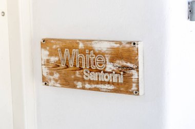 Kırsal ahşap tabela ve beyaz yıkanmış metin okumaları. ini, Yunanistan 'ın Imerovigli kentinde bir Cycladic butik otelinde parlak beyaz bir duvara monte edilmiş.