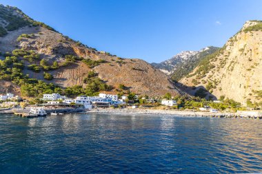 Girit, Yunanistan - 18 Ekim 2024: Samiriye Boğazı eteklerindeki sahil köyünün panoramik görüntüleri, mavi sular, beyaz binalar ve çevresindeki dağ manzarası