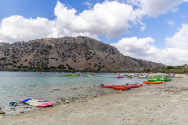 Heraklion, Yunanistan - 17 Ekim 2024: Kournas Gölü 'nde canlı bir gün: Girit Dağlarının Altındaki Kıyıda Renkli Kano Hattı.